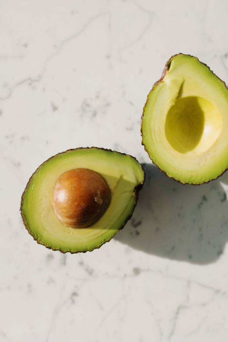 Top view of halved tasty avocado with seed placed on white marble table