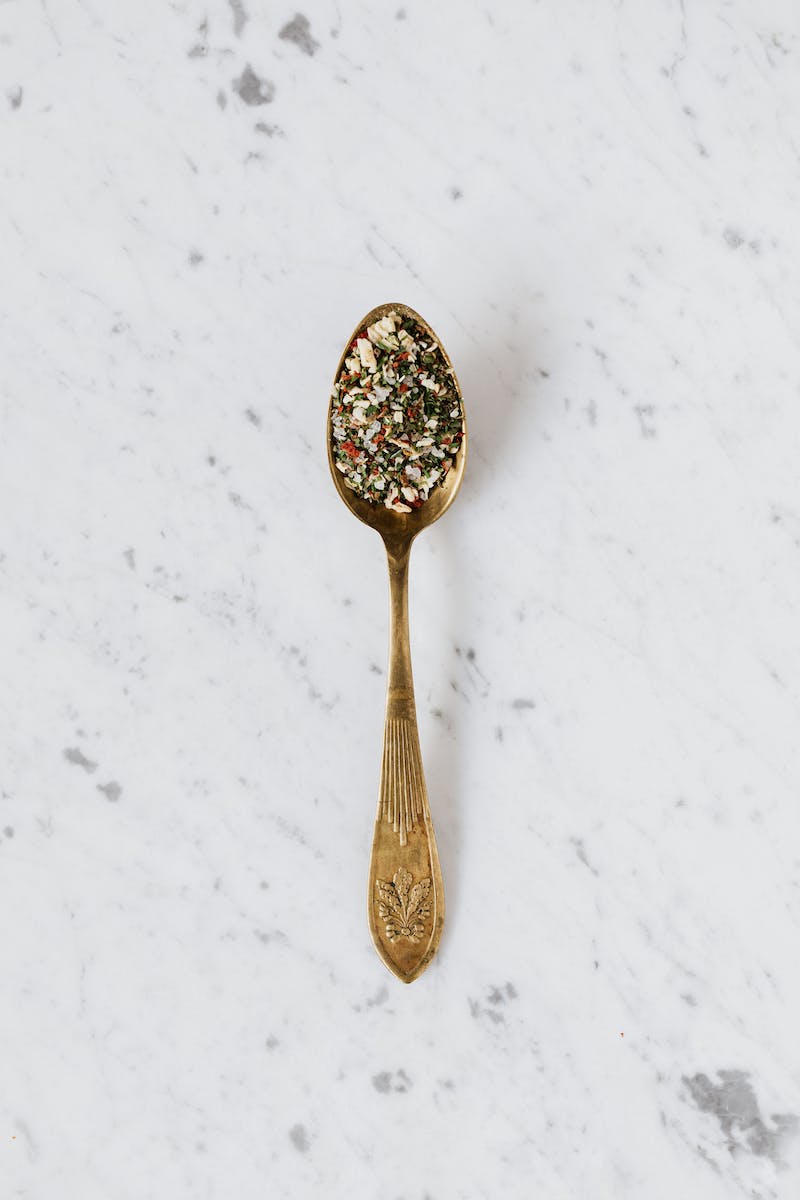 Top view of metal spoon filled with mixed herbs and spices used for healthy gourmet food preparing placed on marble surface