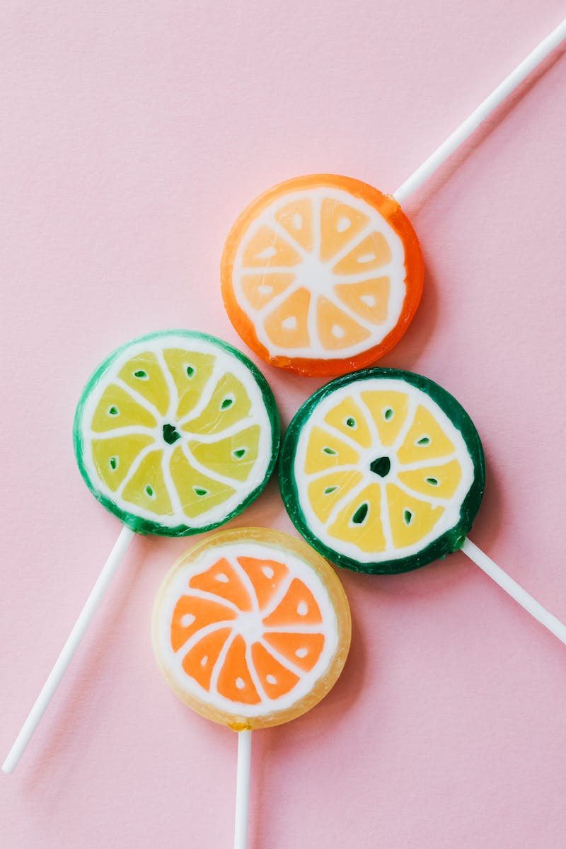 From above of round shaped colorful candies similar to citrus fruits on plastic sticks on pink surface