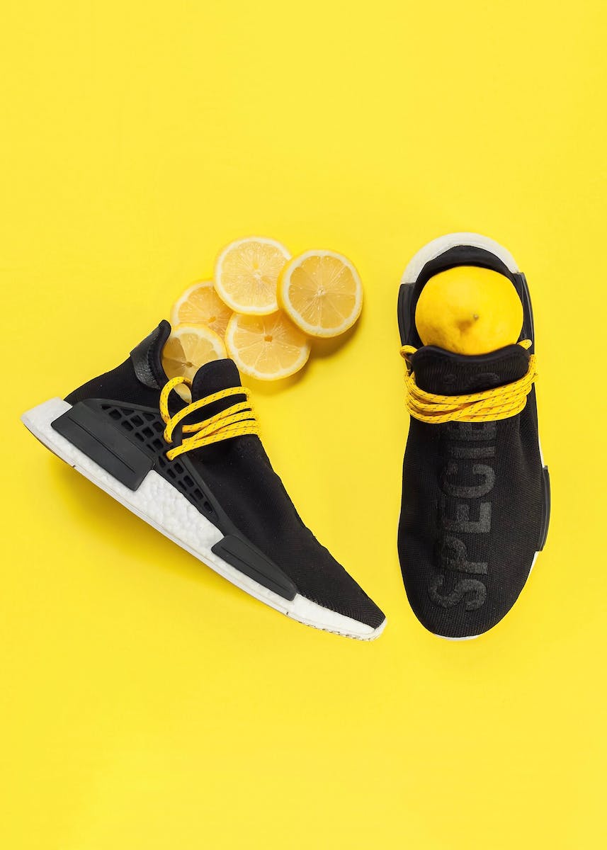 Top view of pair of trendy black trainers with white outsole placed on yellow surface with fresh natural lemons