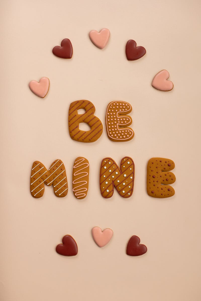 Top view of cookies forming Be Mine phrase on beige background in studio with heart shaped sweets during holiday celebration