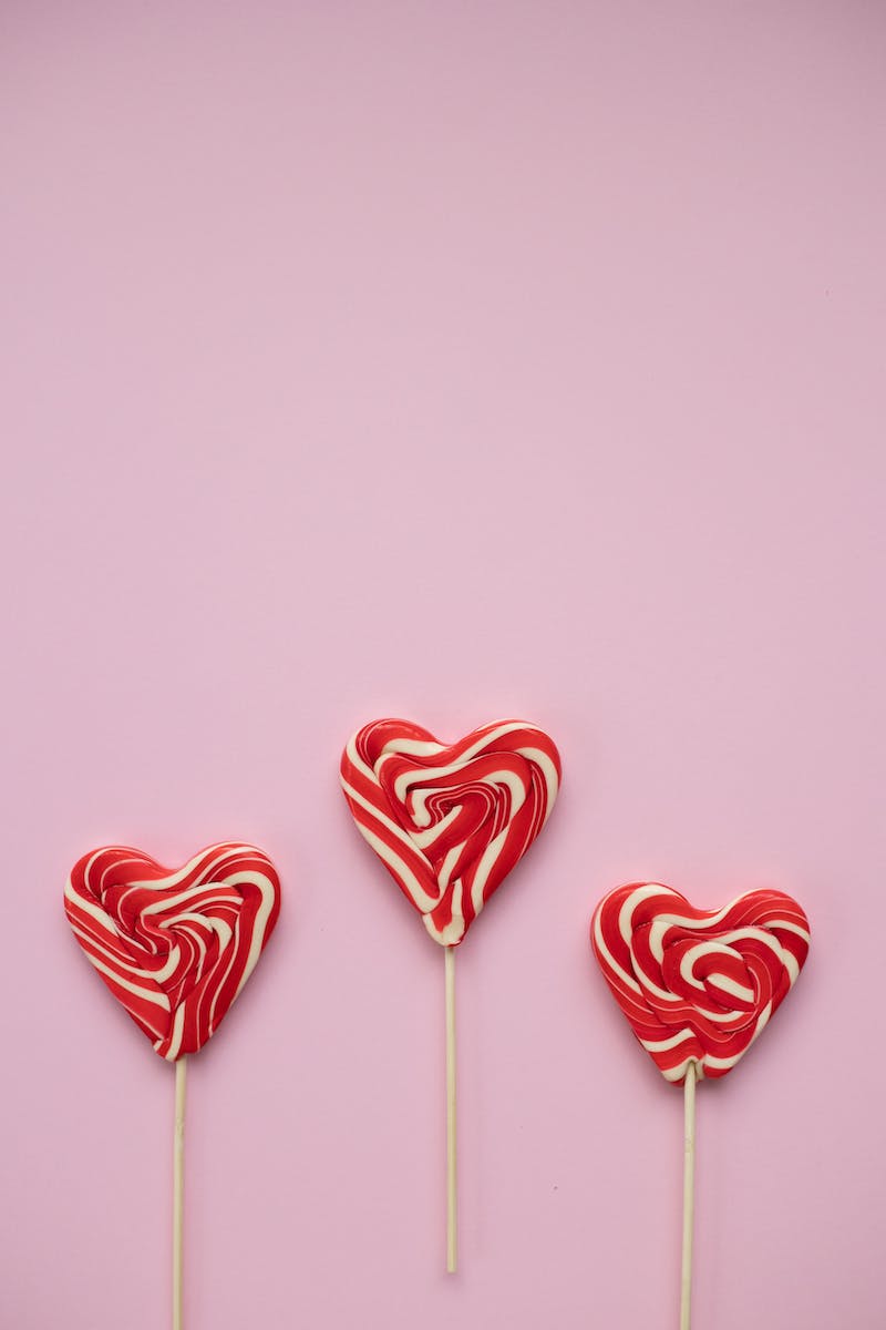 From above of tasty colourful lollipops in form of hearts placed on pink background