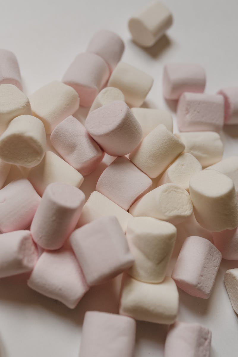 From above delicious yummy light marshmallows in cylindrical shapes scattered on white table