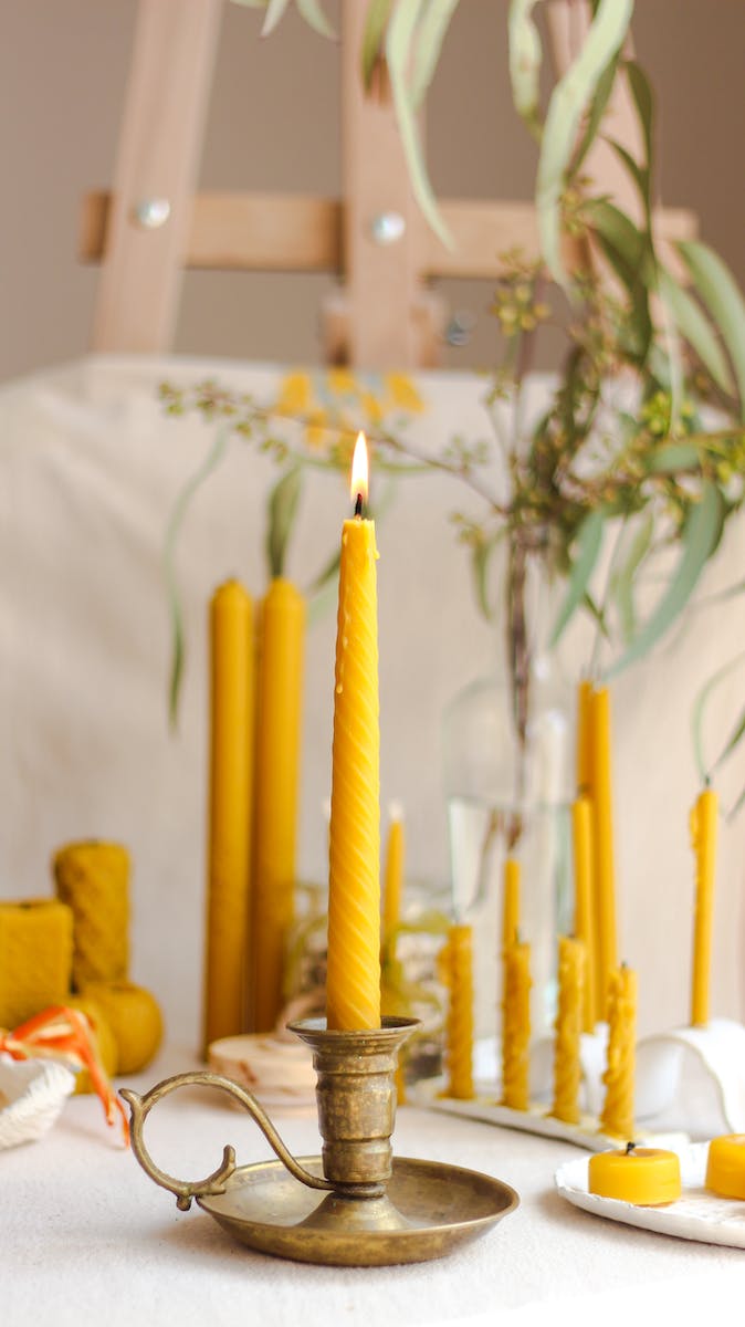 Old metal candlestick with flaming wax candle against plant leaf in light house on blurred background