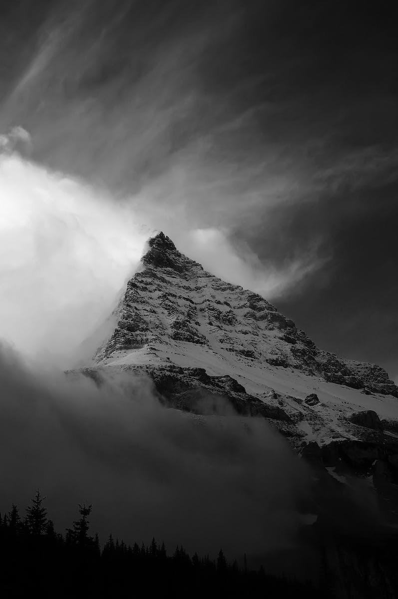 Grayscale Photo of Snow Covered Mountain under a Cloudy Sky
