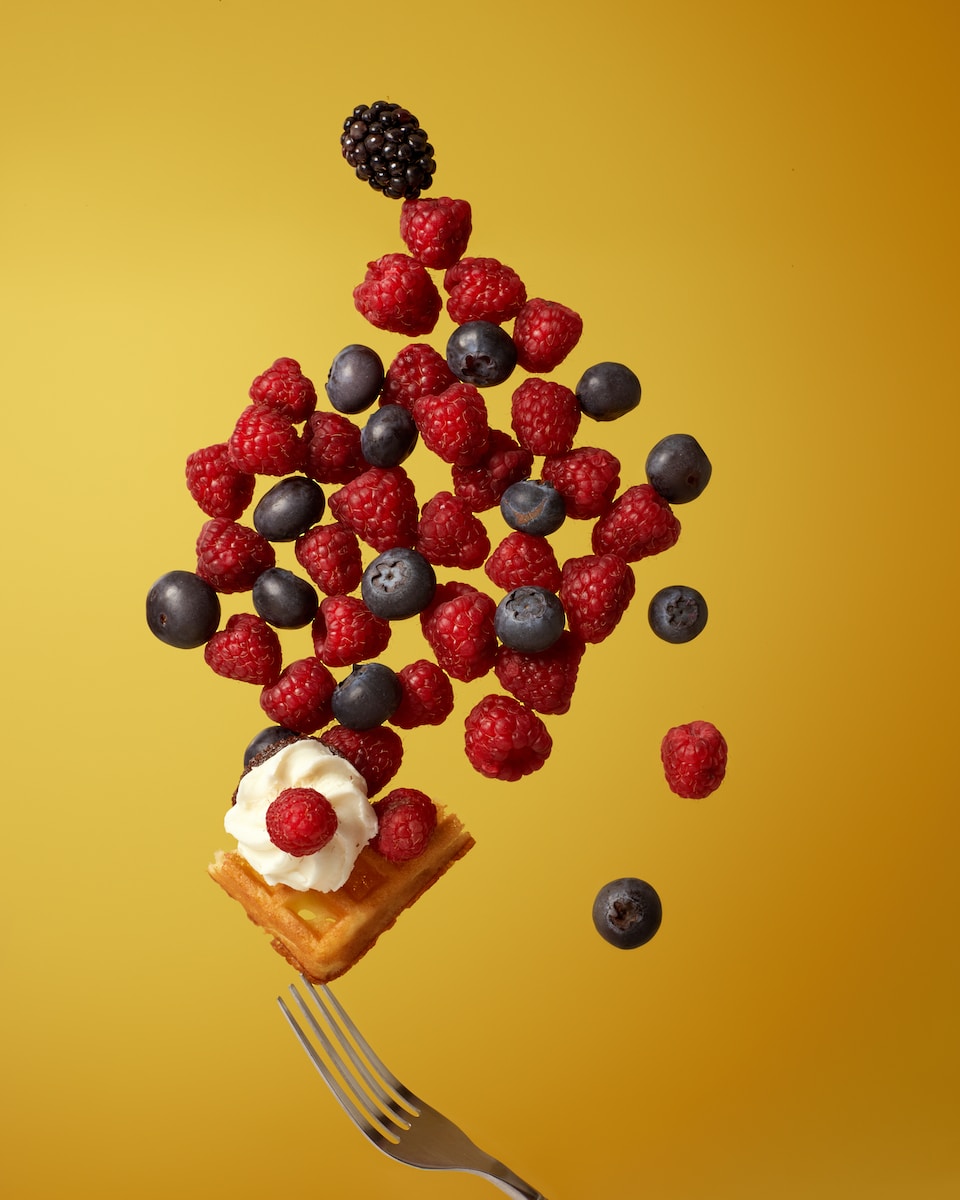 a piece of cake on a fork with berries and blueberries falling out of it