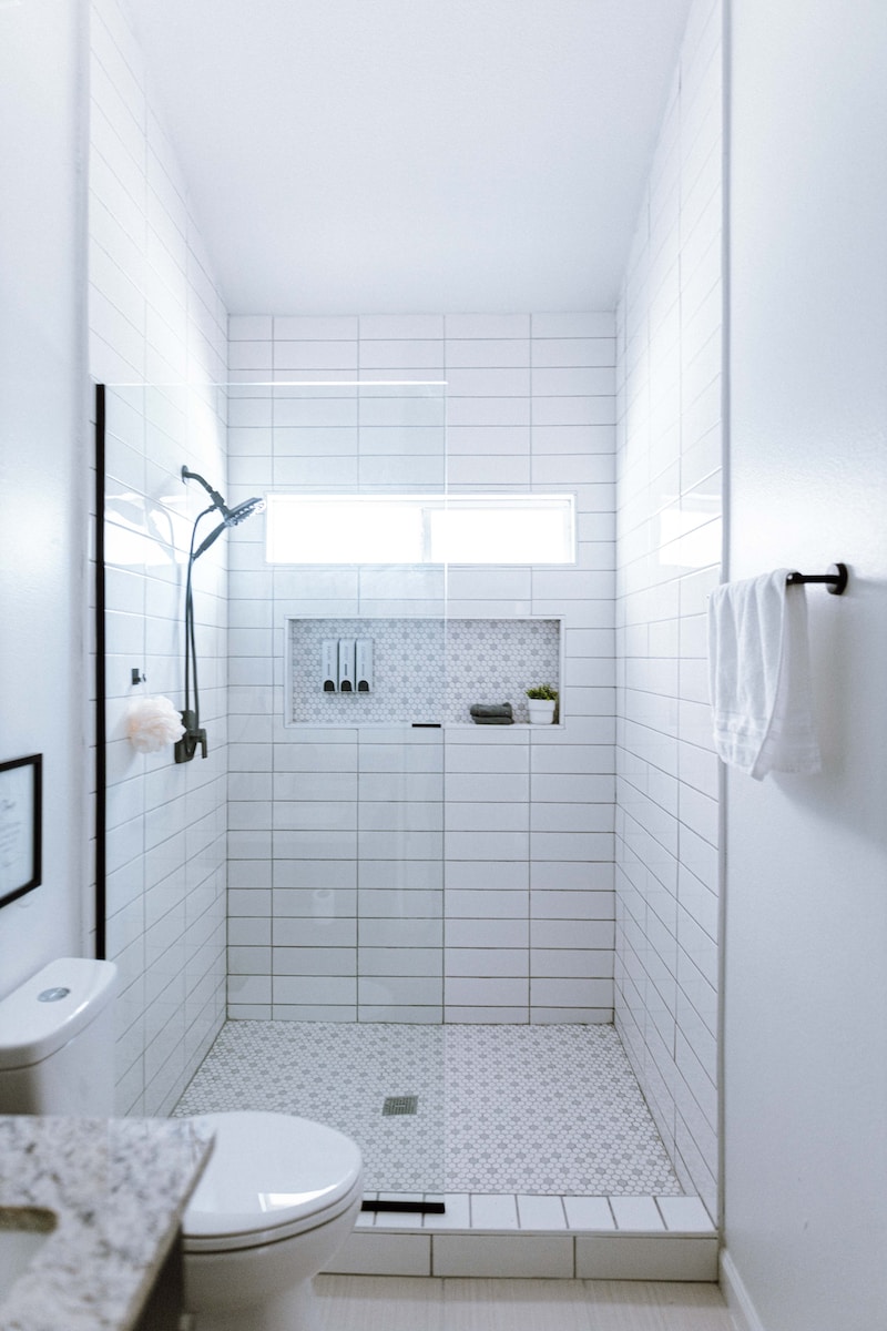 a white tiled bathroom with a shower and toilet