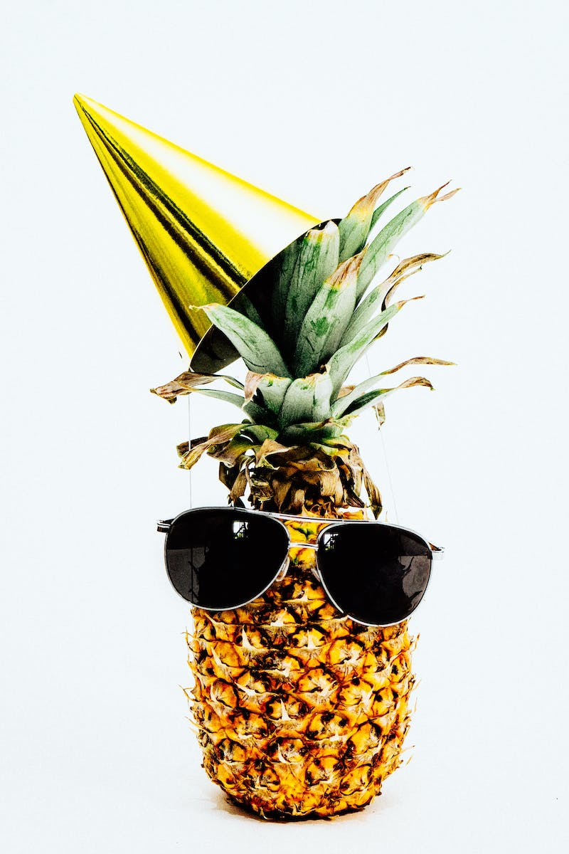 Close-up Photo of Pineapple with Party Hat and a Black Sunglasses