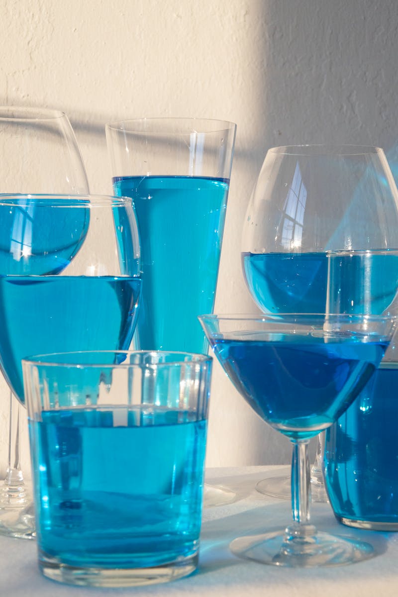 Composition of different crystal glasses filled with light blue beverage placed on table