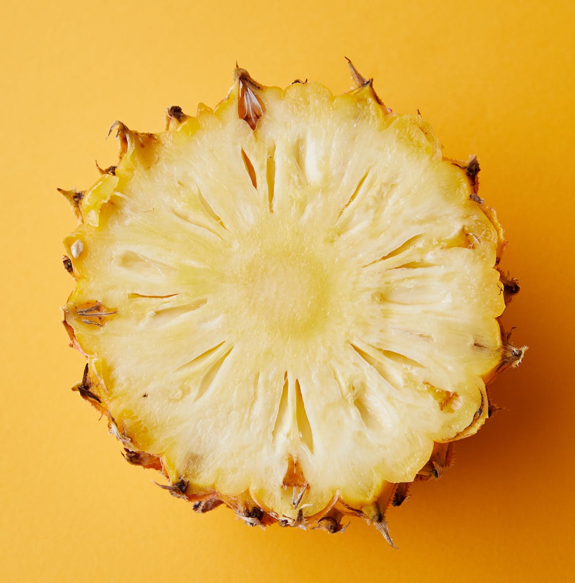 Top view half of appetizing ripe juicy exotic pineapple placed on yellow background