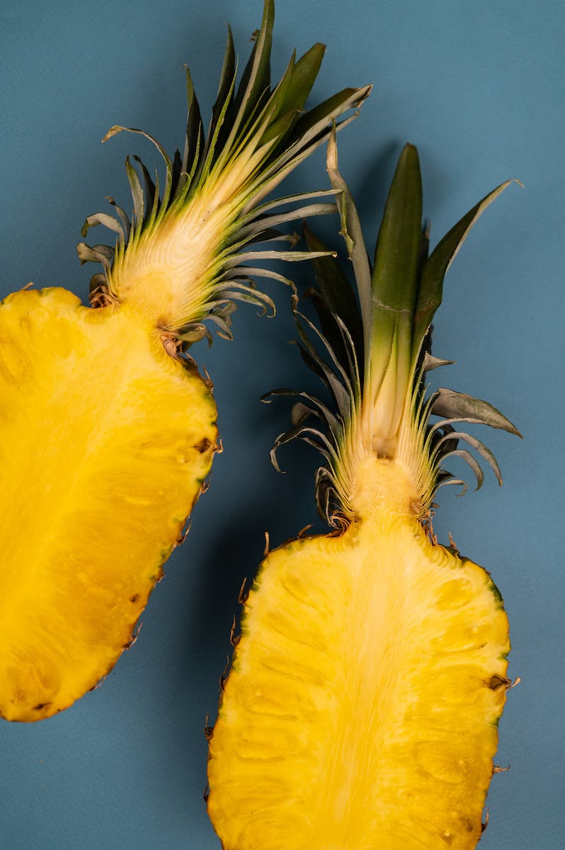 Top view of delicious fresh pineapple halves with yellow flesh and curved leaves on blue background