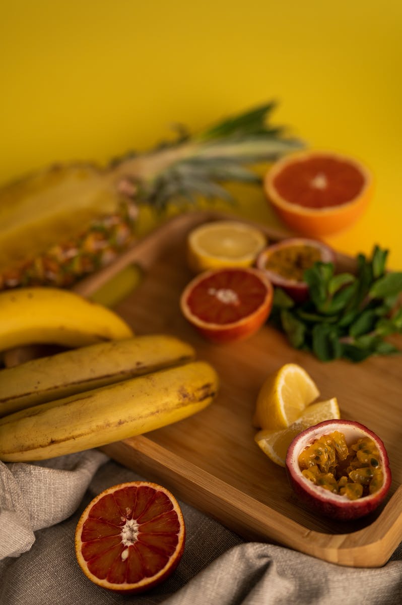 Delicious fresh citrus fruits and ripe passion fruit and halved pineapple with banana and mint on wooden board with cloth on yellow background