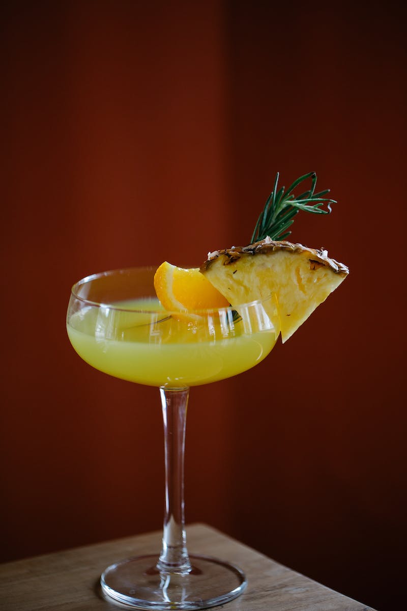 Glass of Yellow Cocktail with Fruits against Dark Red Background