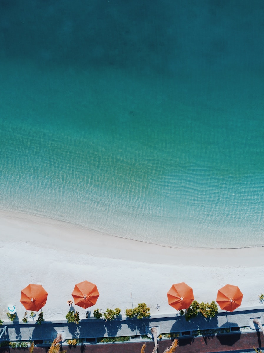 aerial photography of four orange patio umbrellas on seashore