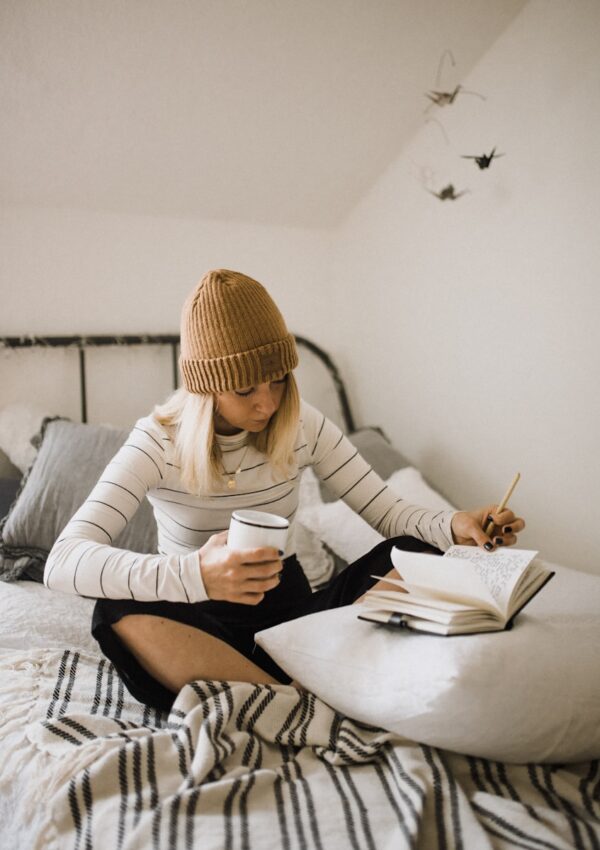 woman in striped shirt sitting on bed while writing